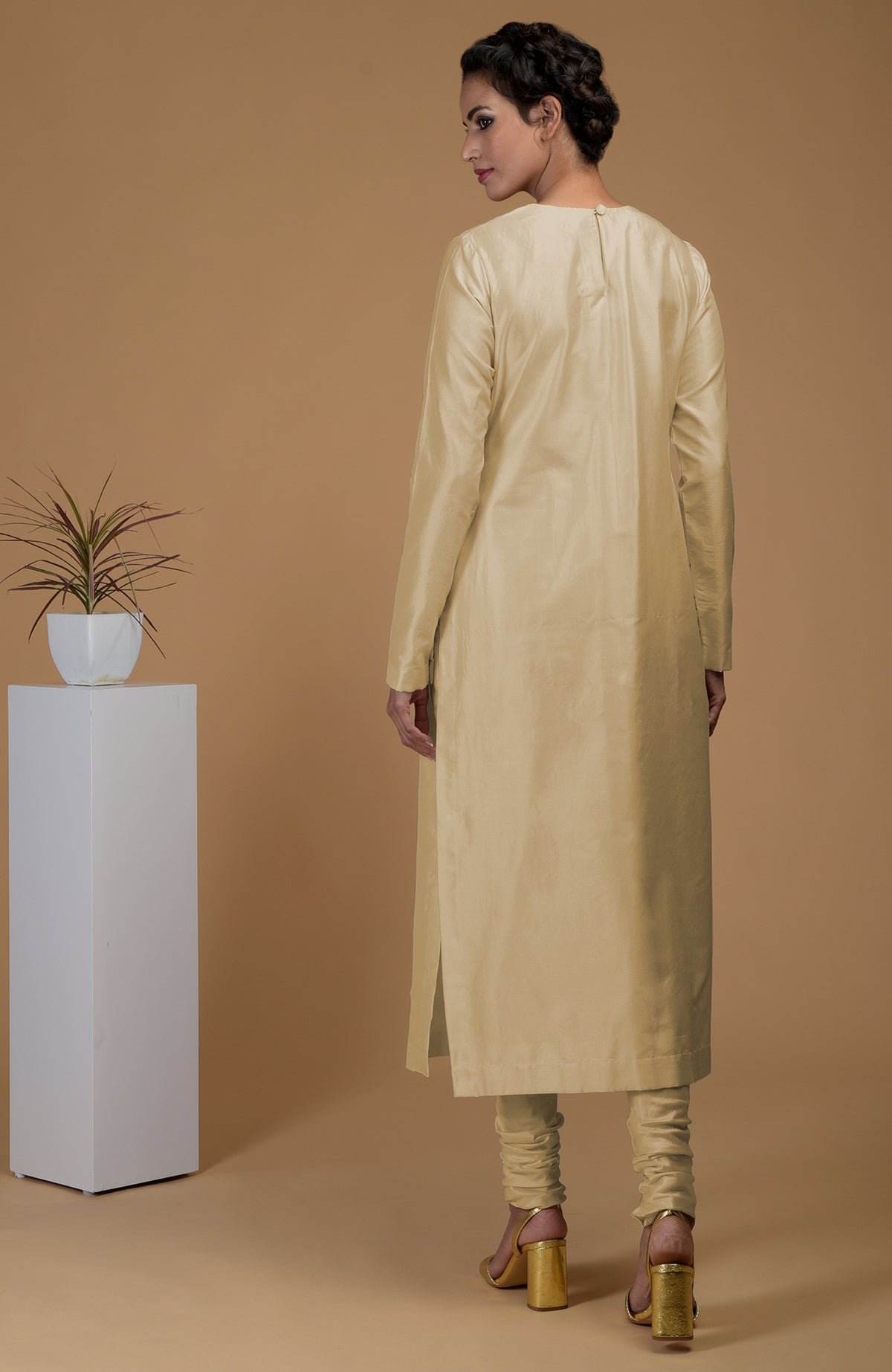 A woman models a beige pure Matka silk kurta set with a jewel neck and churidars.