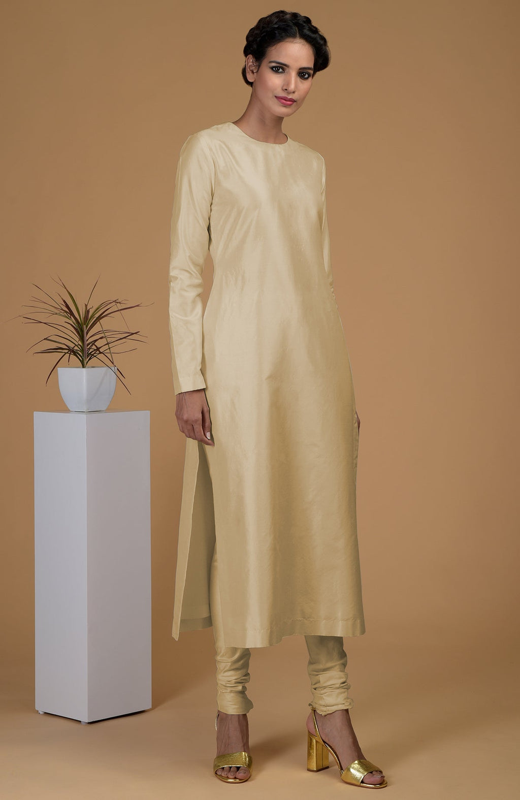 A woman models a beige pure Matka silk jewel neck kurta set with gold heels.