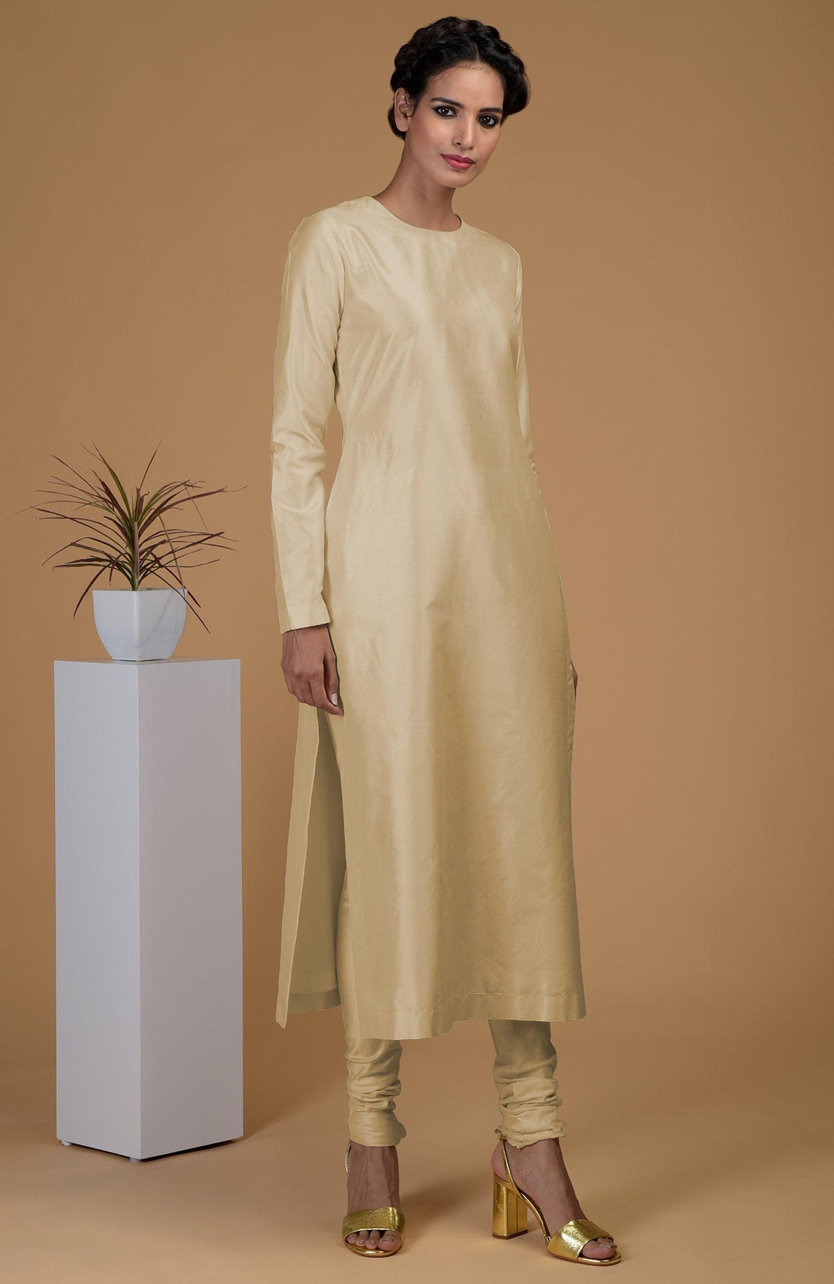 A woman models a beige pure Matka silk jewel neck kurta set with gold heels.