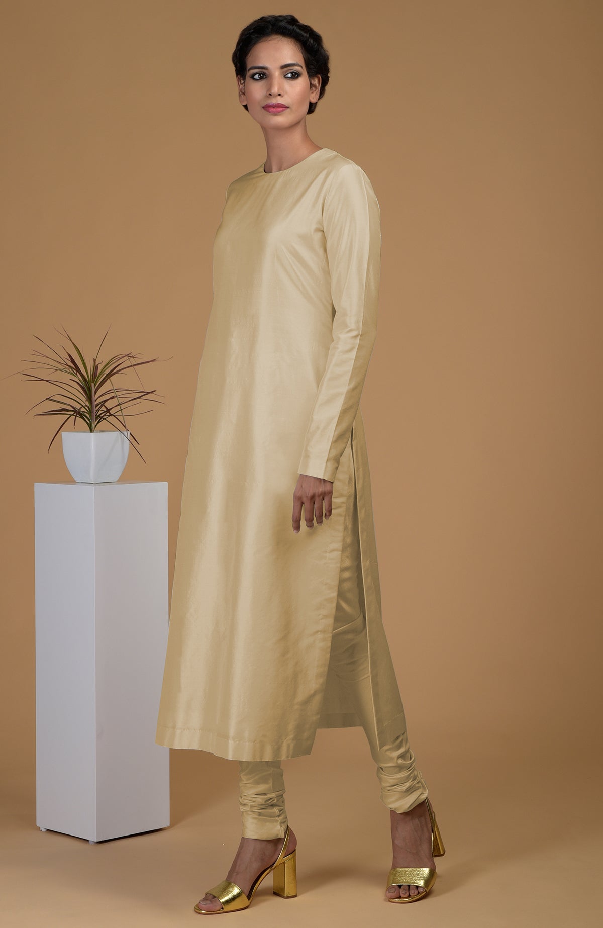 A woman models a beige pure Matka silk kurta set with gold heels.