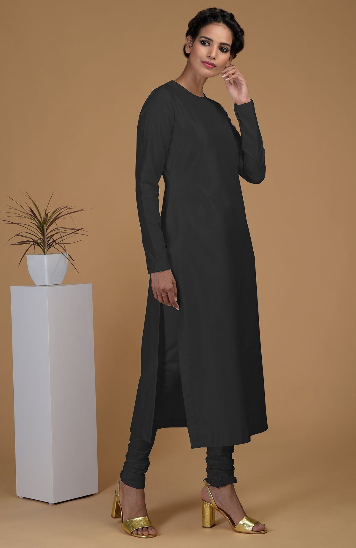 A woman models a black pure Matka silk jewel neck kurta set with gold heels.