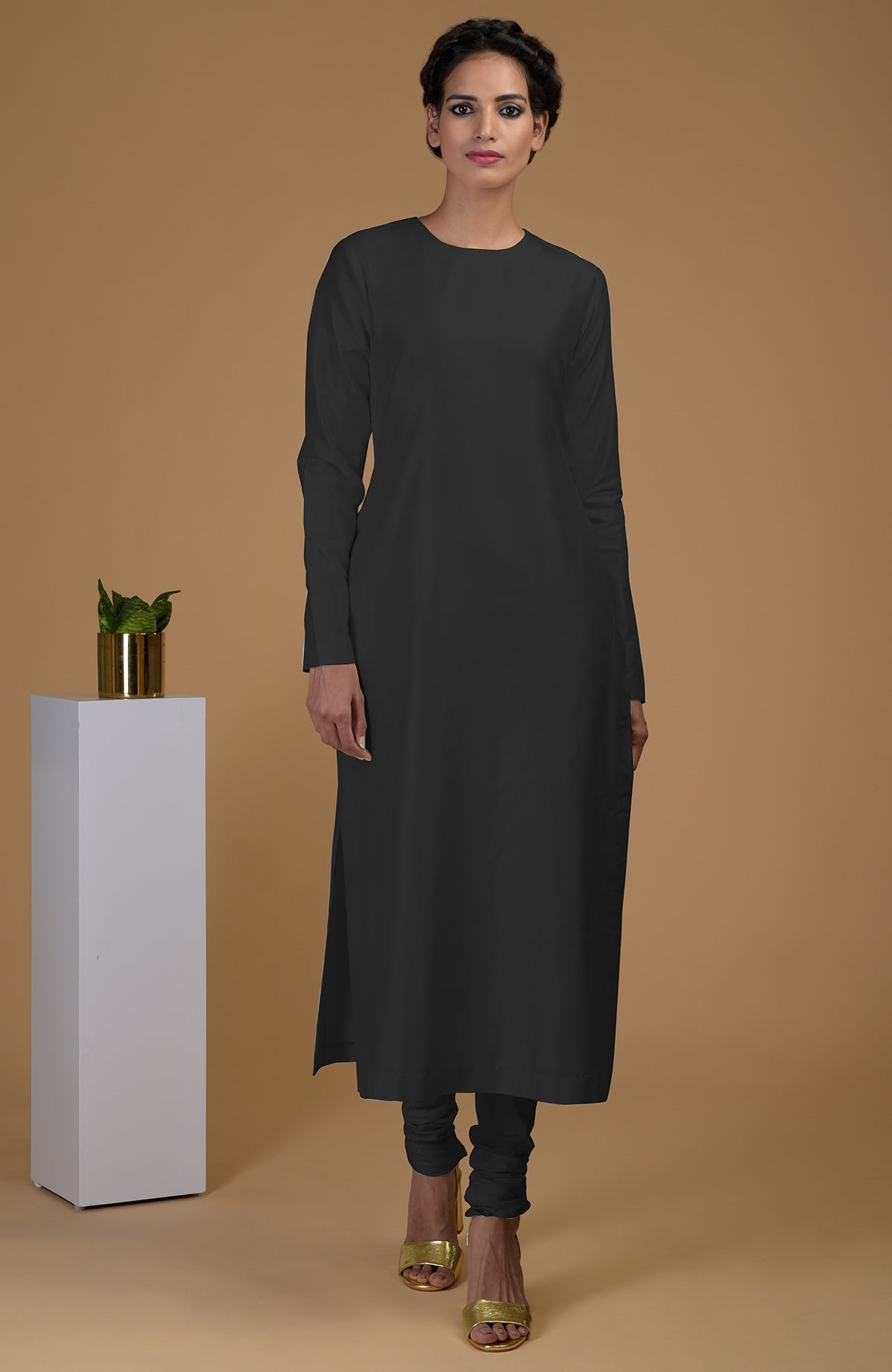 A woman models a black pure Matka silk jewel neck kurta set with churidars.