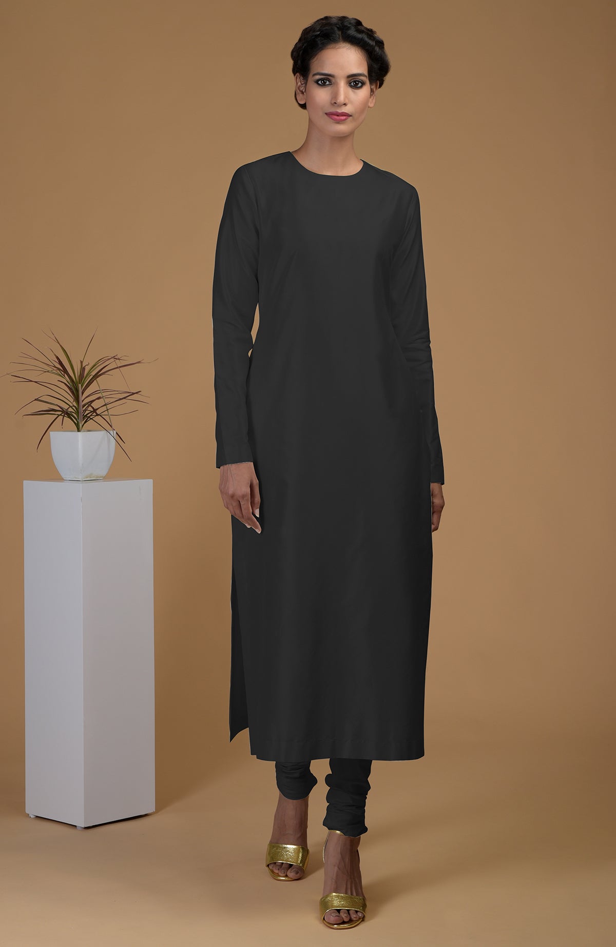 A woman models a black pure Matka silk jewel neck kurta set with gold heels.