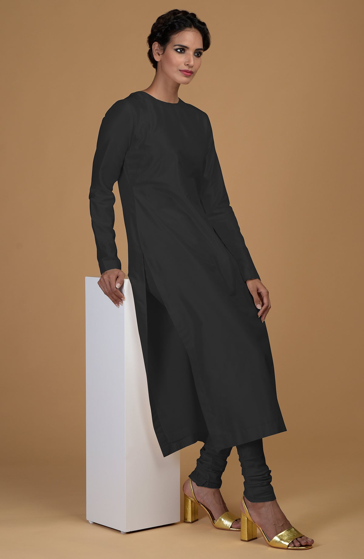 A woman models a black pure Matka silk kurta set with gold heels.
