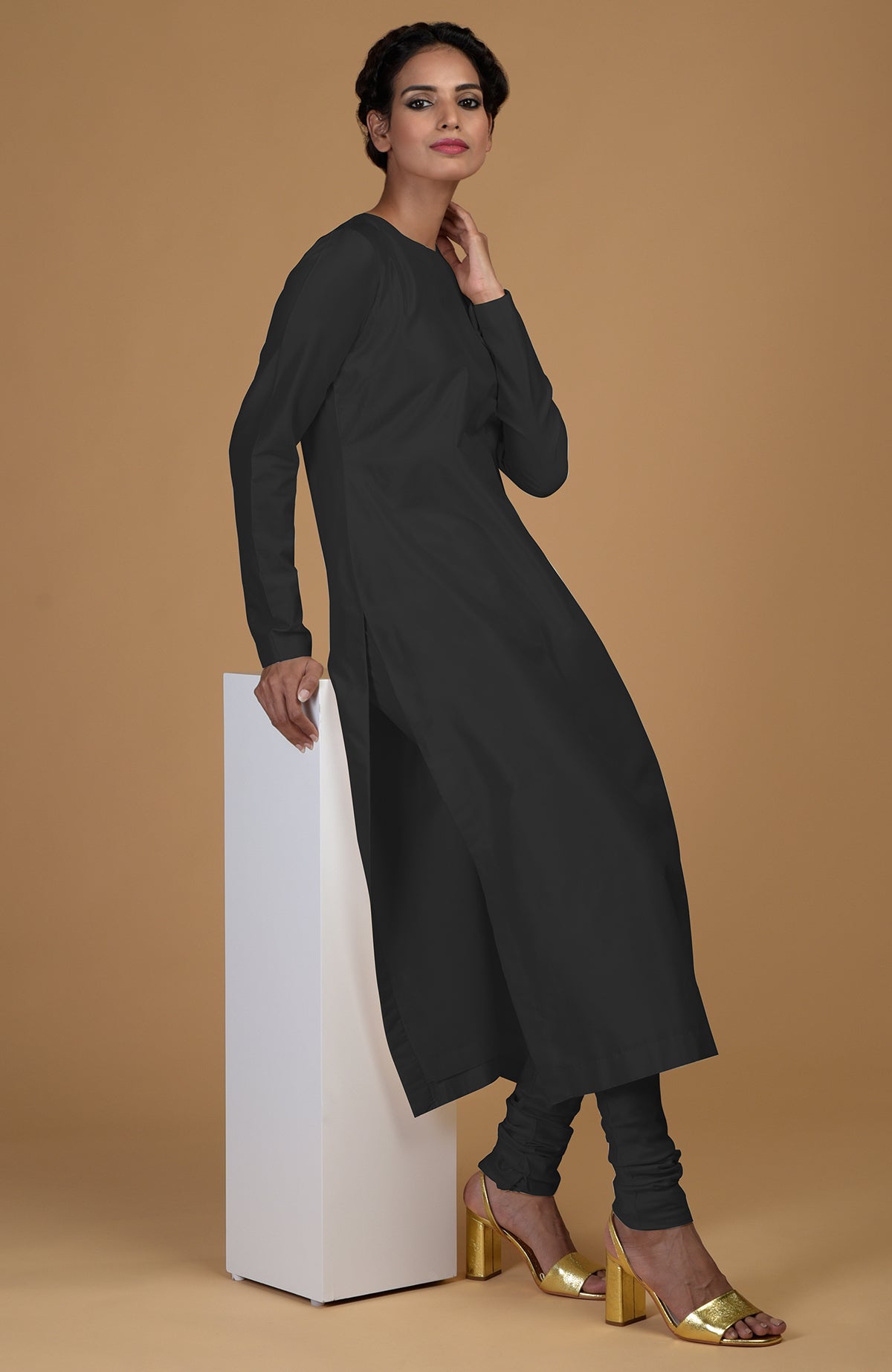 A woman models a black pure Matka silk kurta set with gold heels.