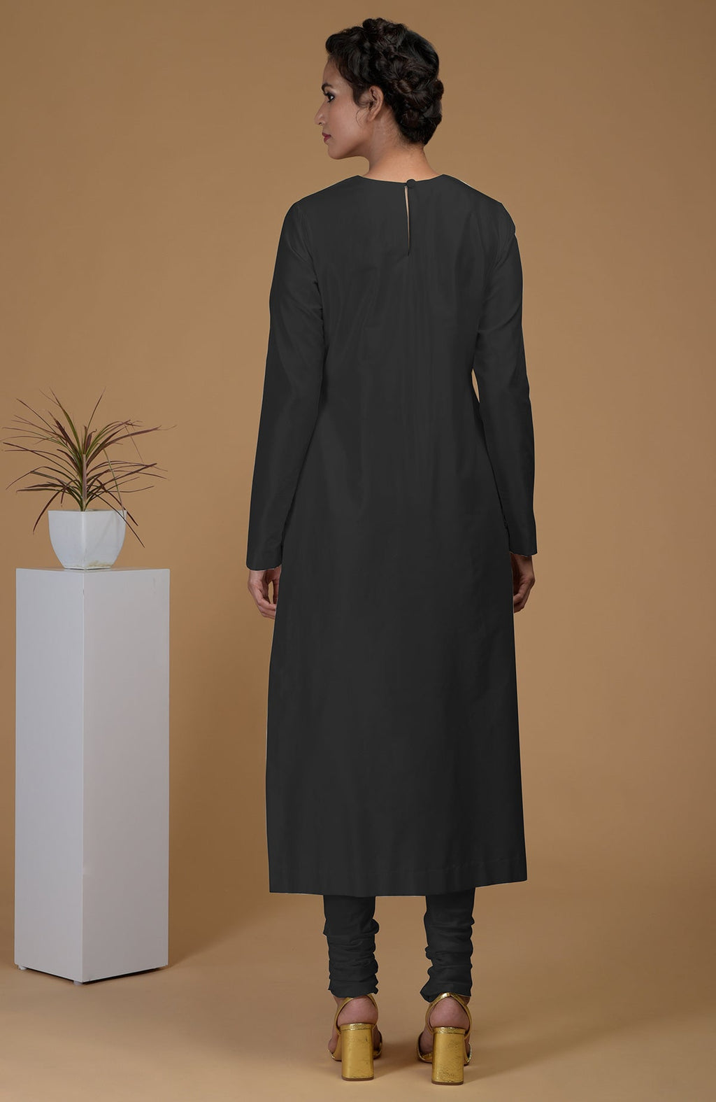 A woman models a black pure Matka silk kurta set with a jewel neck and churidars.