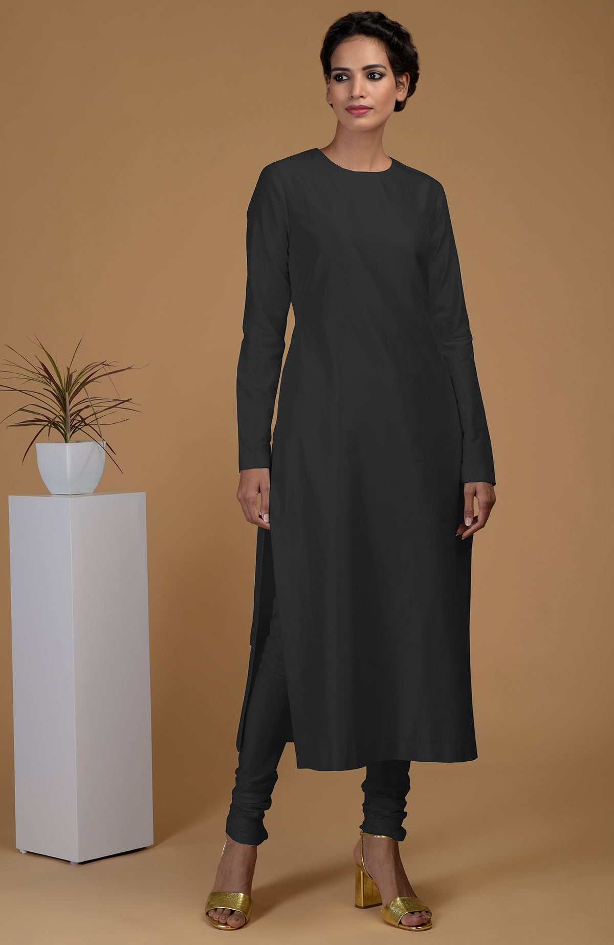 A woman models a black pure Matka silk jewel neck kurta set with gold heels.