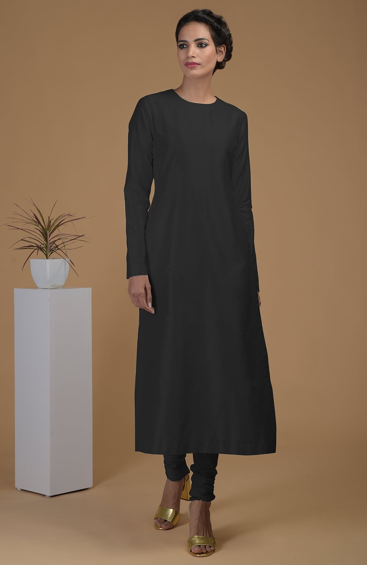A woman models a black pure Matka silk kurta set with churidars and gold heels.