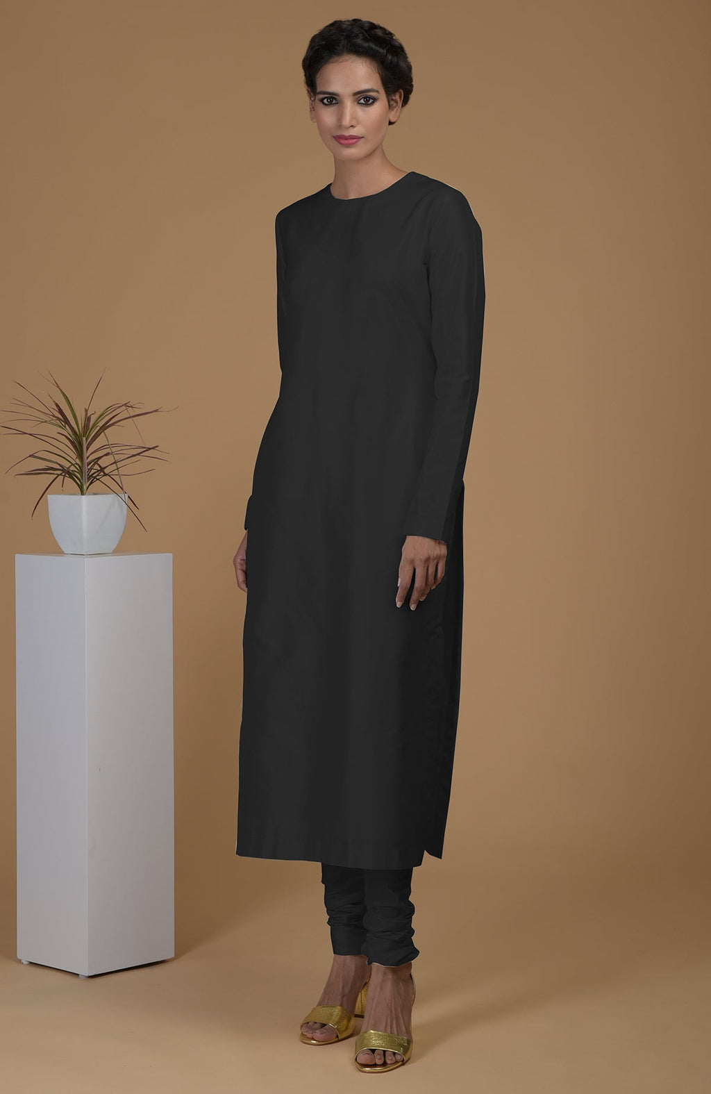 A woman models a black pure Matka silk jewel neck kurta set with churidars.