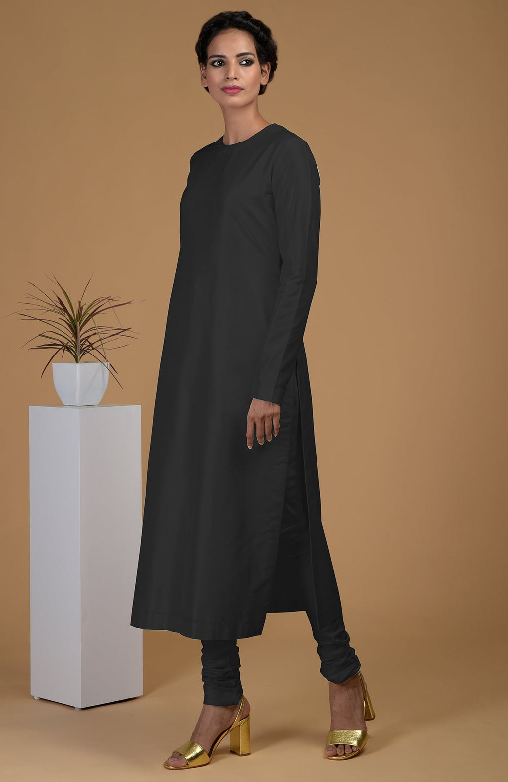 A woman models a black pure Matka silk jewel neck kurta set with golden heels.
