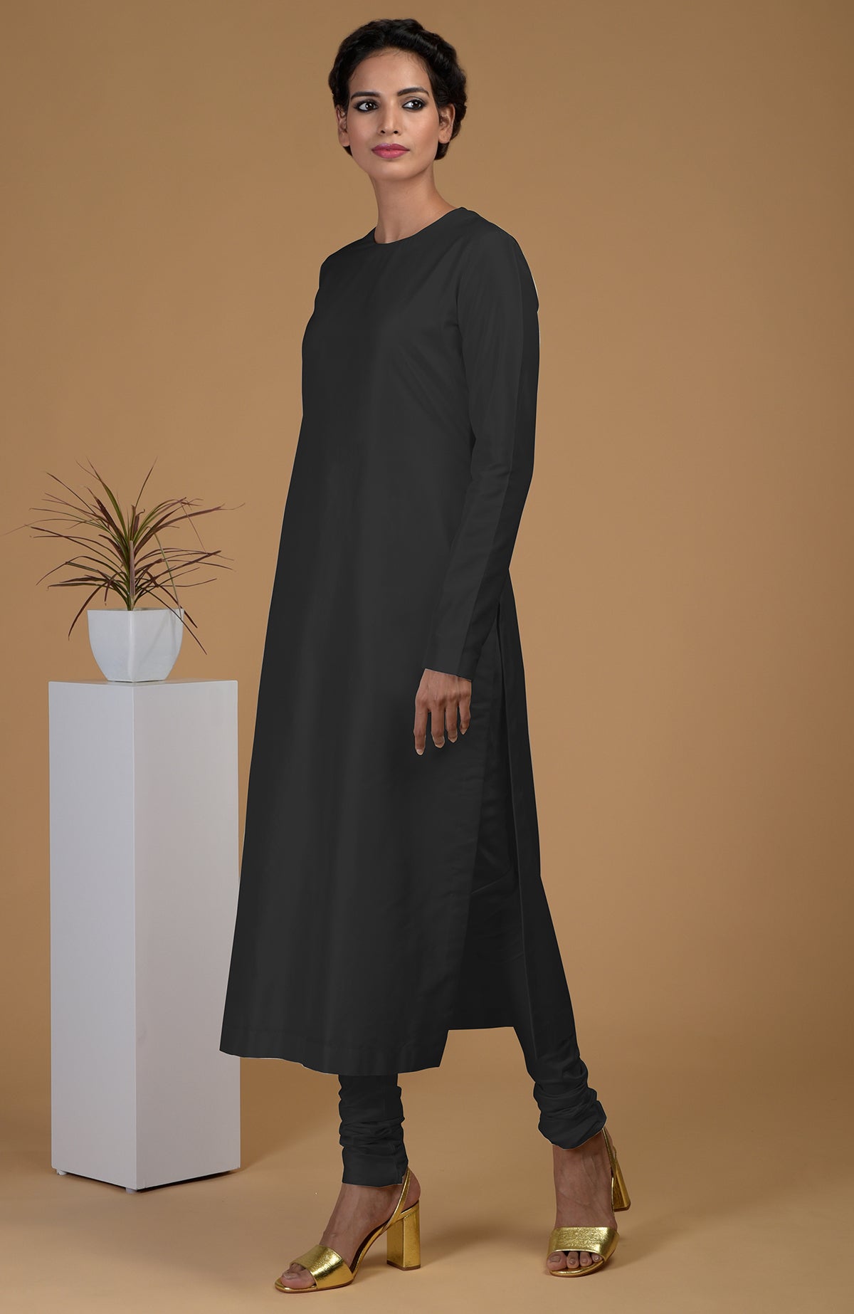A woman models a black pure Matka silk jewel neck kurta set with golden heels.