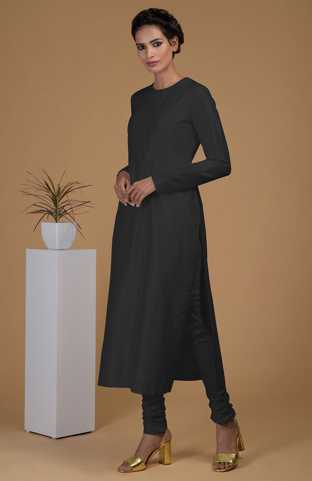 A woman models a black pure Matka silk jewel neck kurta set with gold heels.