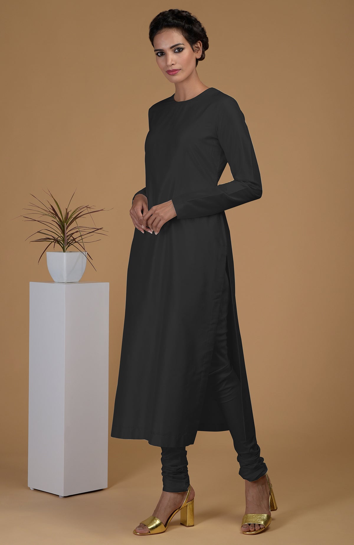 A woman models a black pure Matka silk jewel neck kurta set with gold heels.