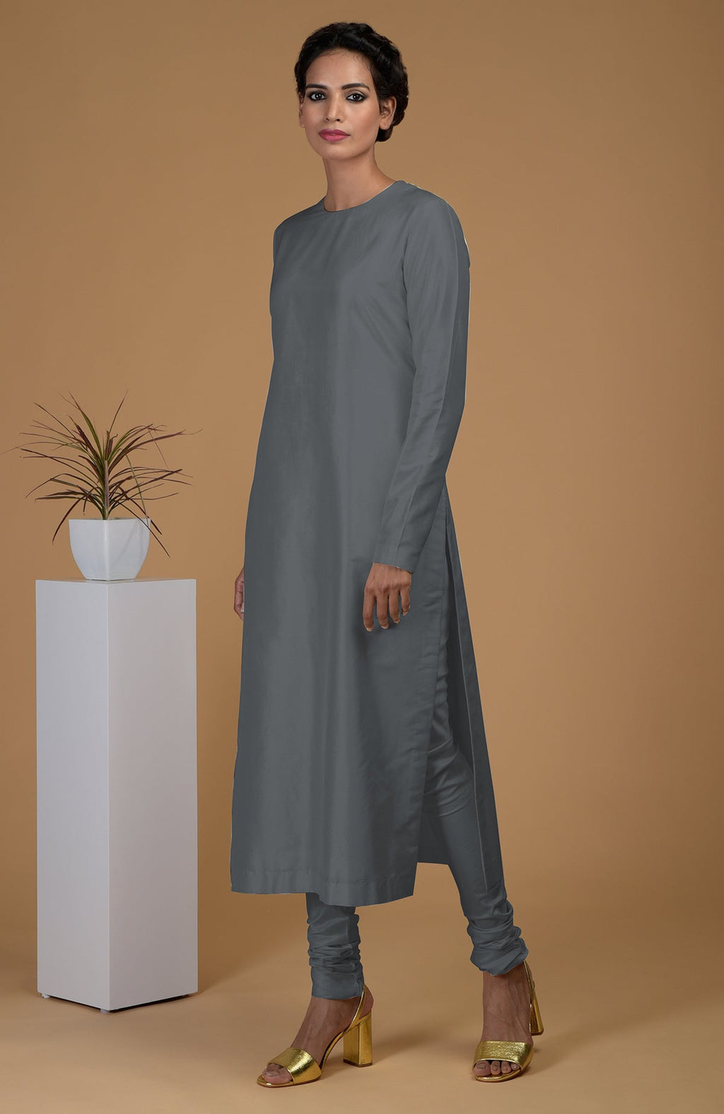 A woman models a grey pure Matka silk kurta set with a jewel neck and churidar pants.
