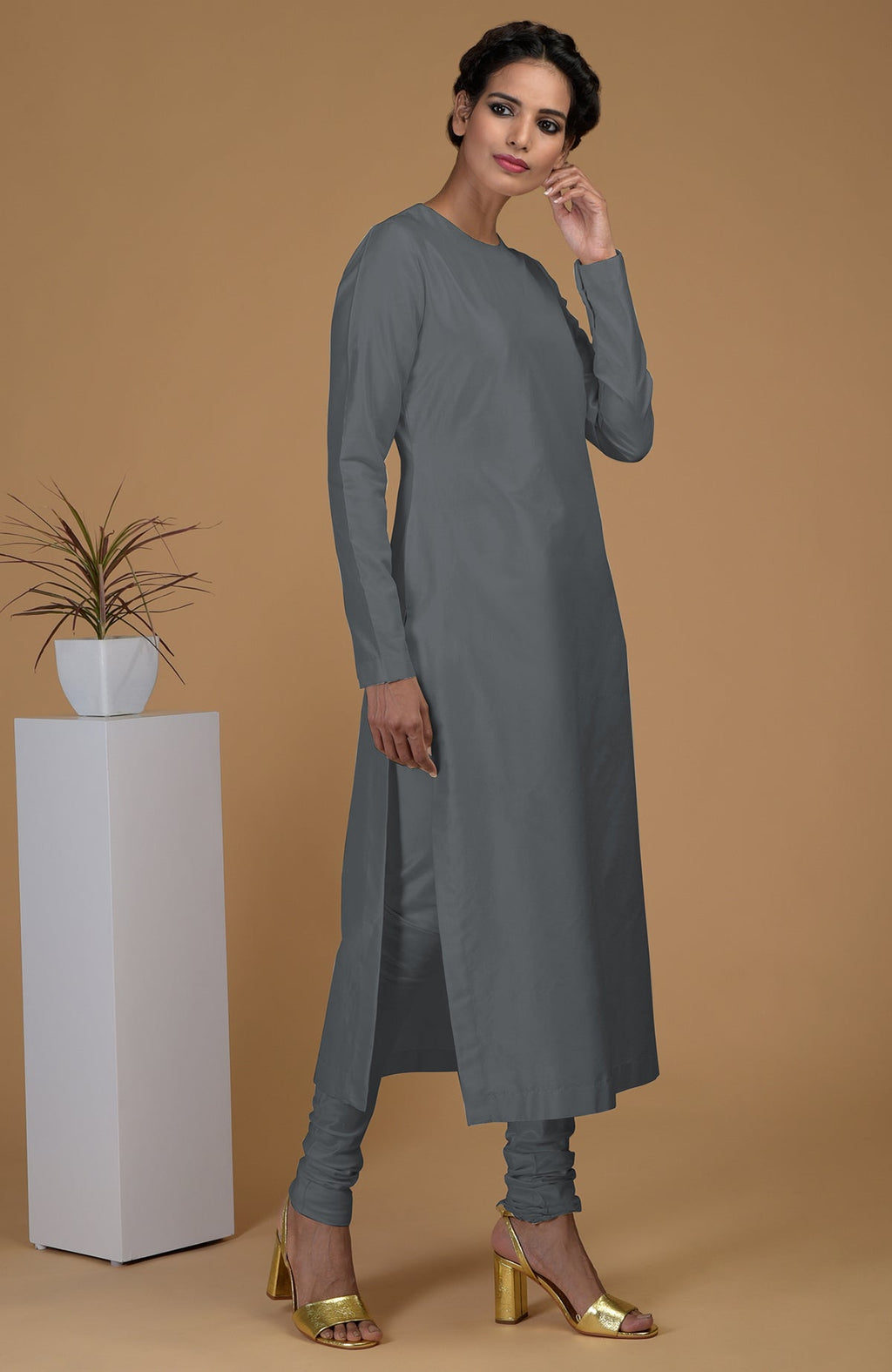 A woman models a grey pure Matka silk jewel neck kurta set with gold heels.