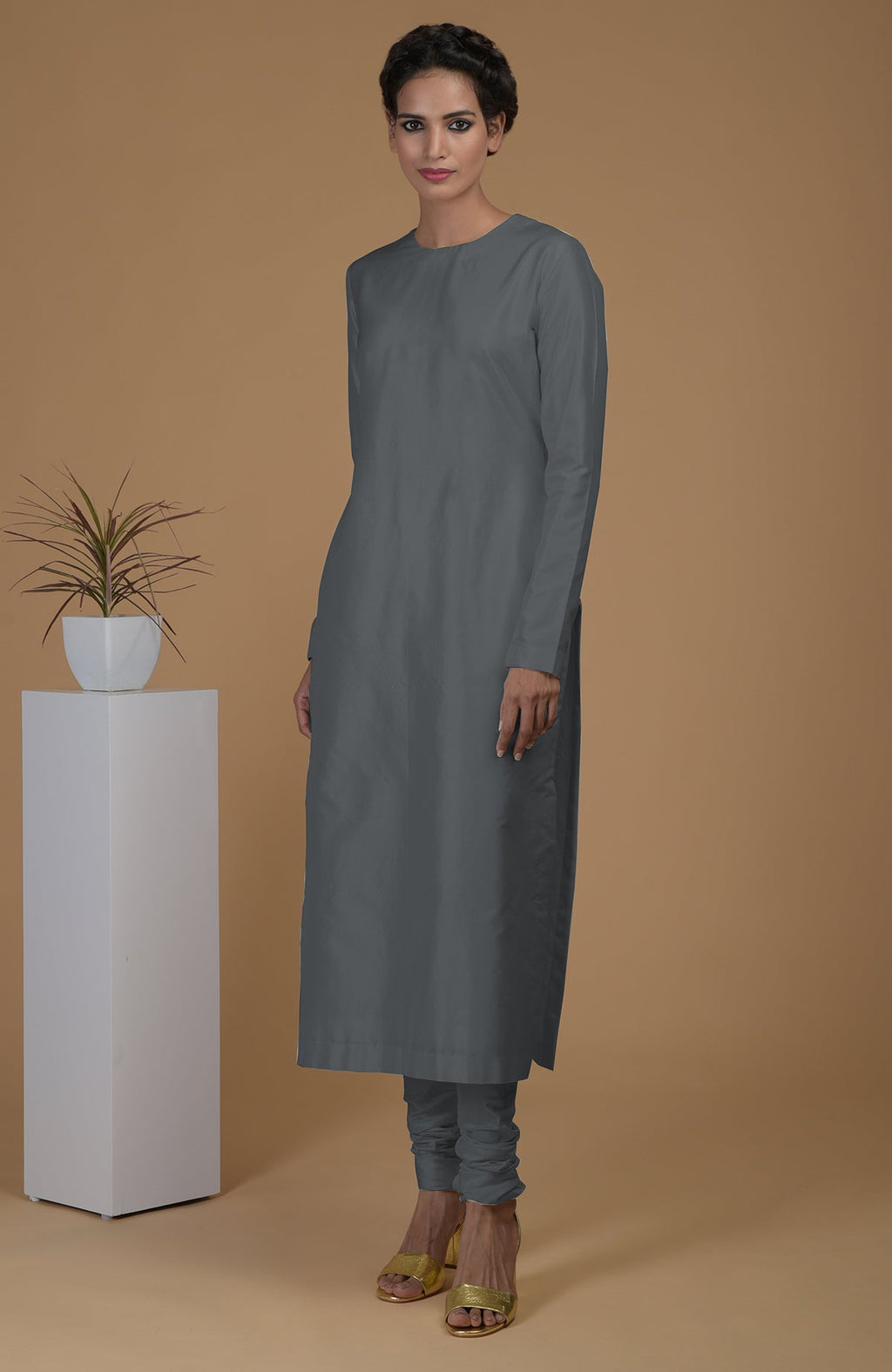 A woman models a grey pure Matka silk jewel neck kurta set with gold heels.