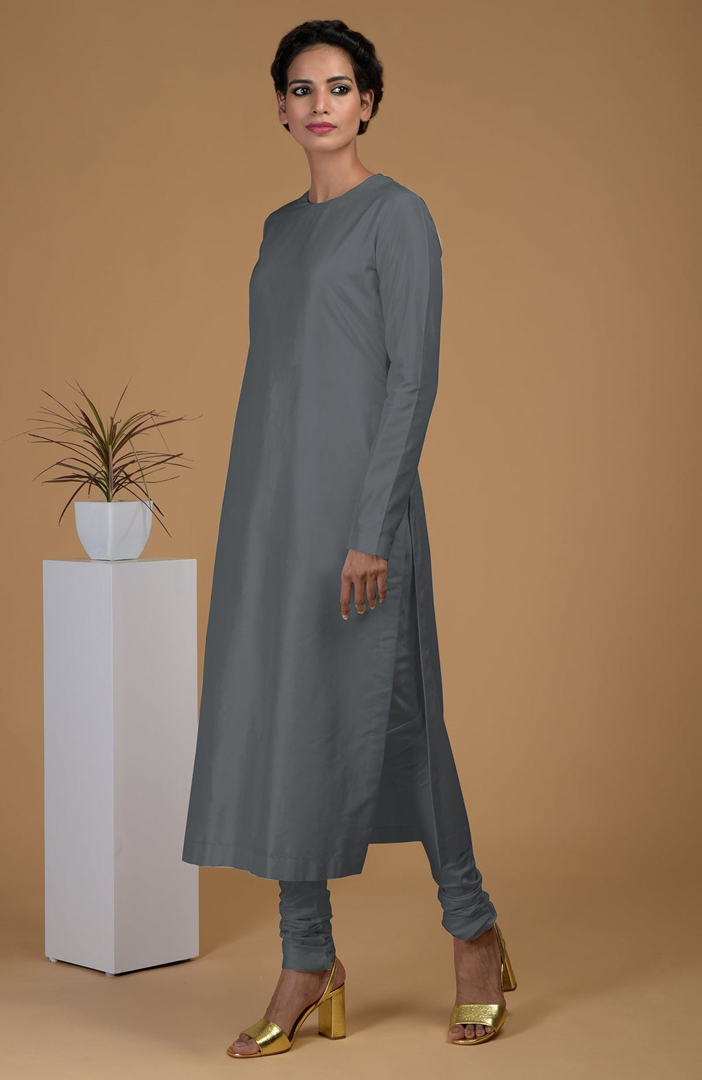 A woman models a grey pure Matka silk jewel neck kurta set with golden heels.