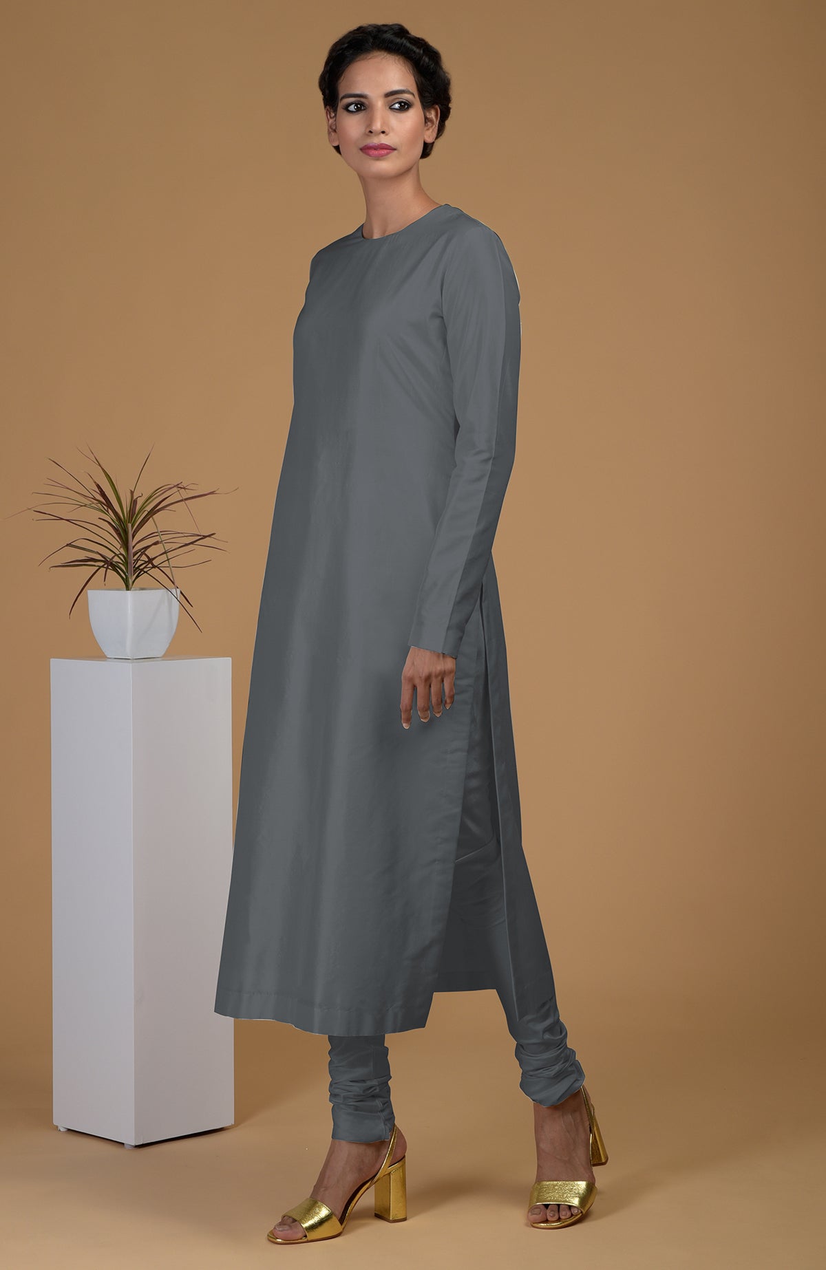 A woman models a grey pure Matka silk jewel neck kurta set with golden heels.