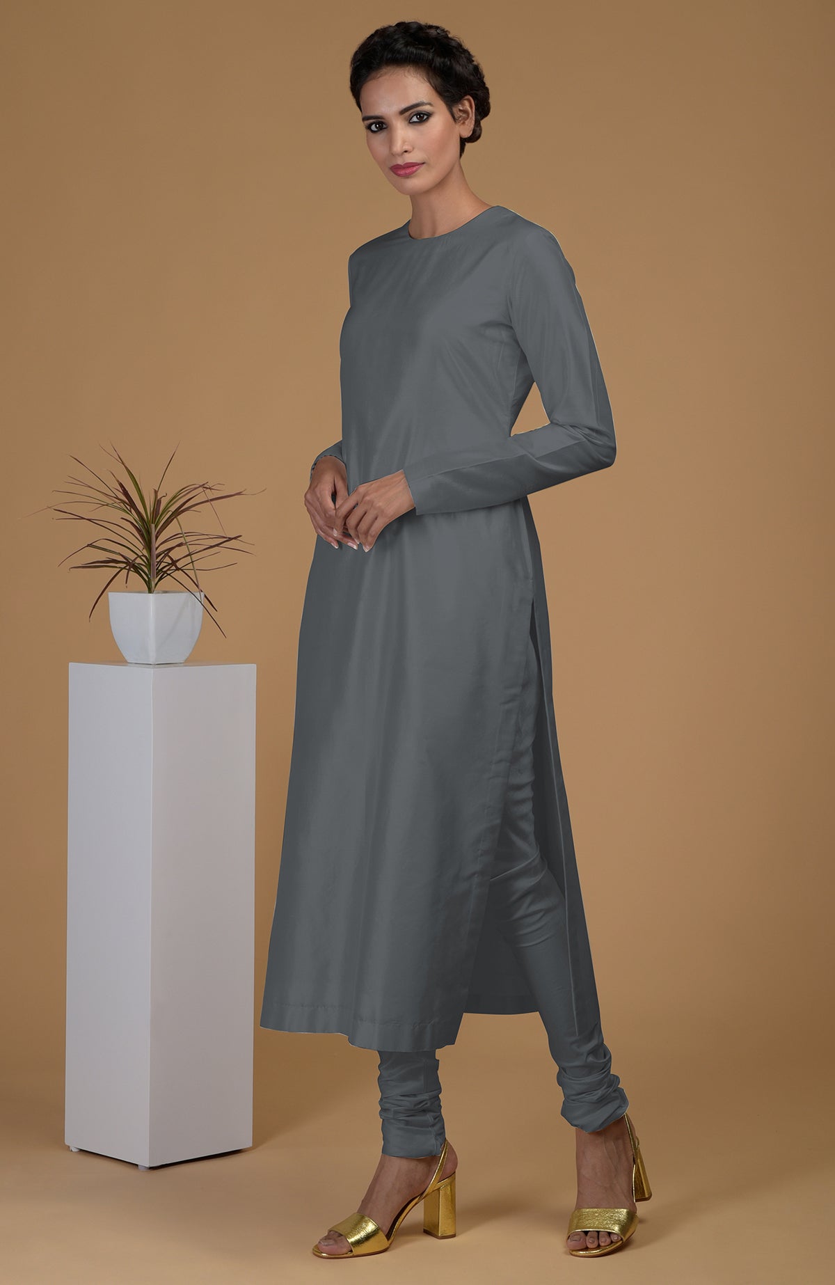 A woman models a grey pure Matka silk jewel neck kurta set with gold heels.