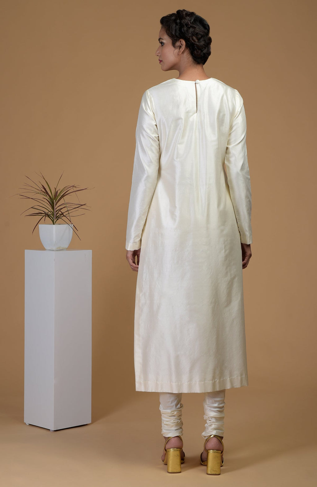 A woman in an ivory Matka silk kurta set with churidars and gold heels.