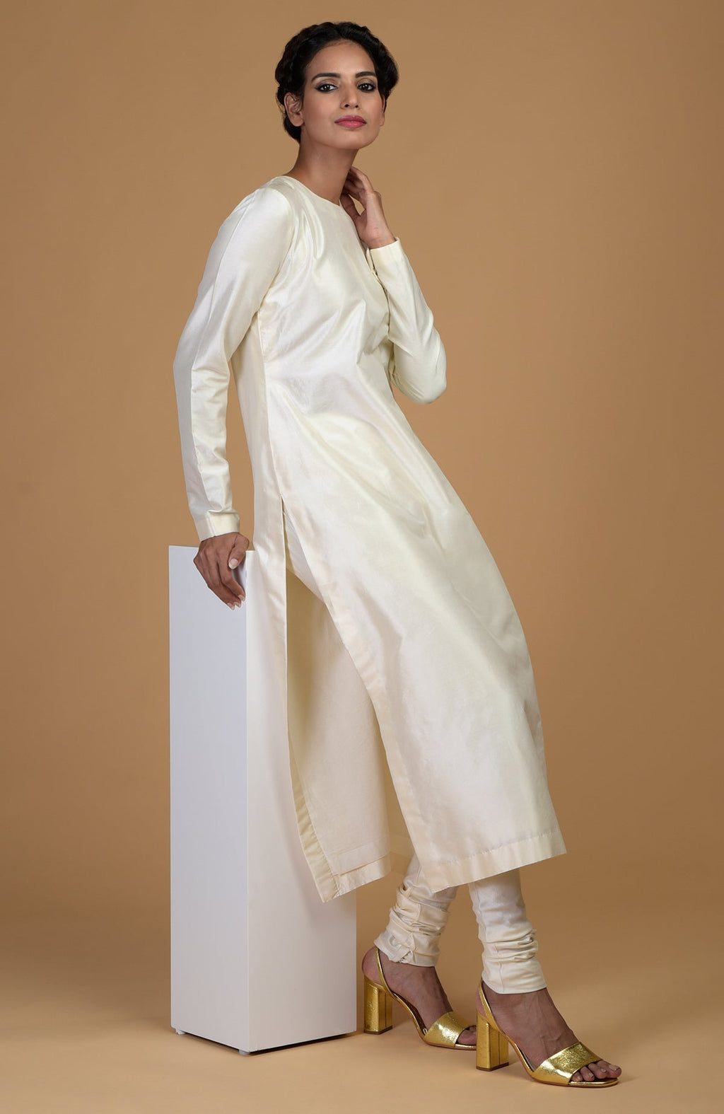 An elegant woman models an ivory pure Matka silk kurta set with golden heels.