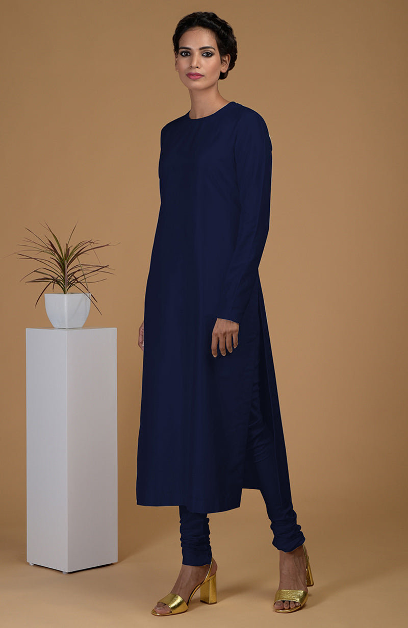 A woman models a navy blue pure Matka silk jewel neck kurta set with golden heels.