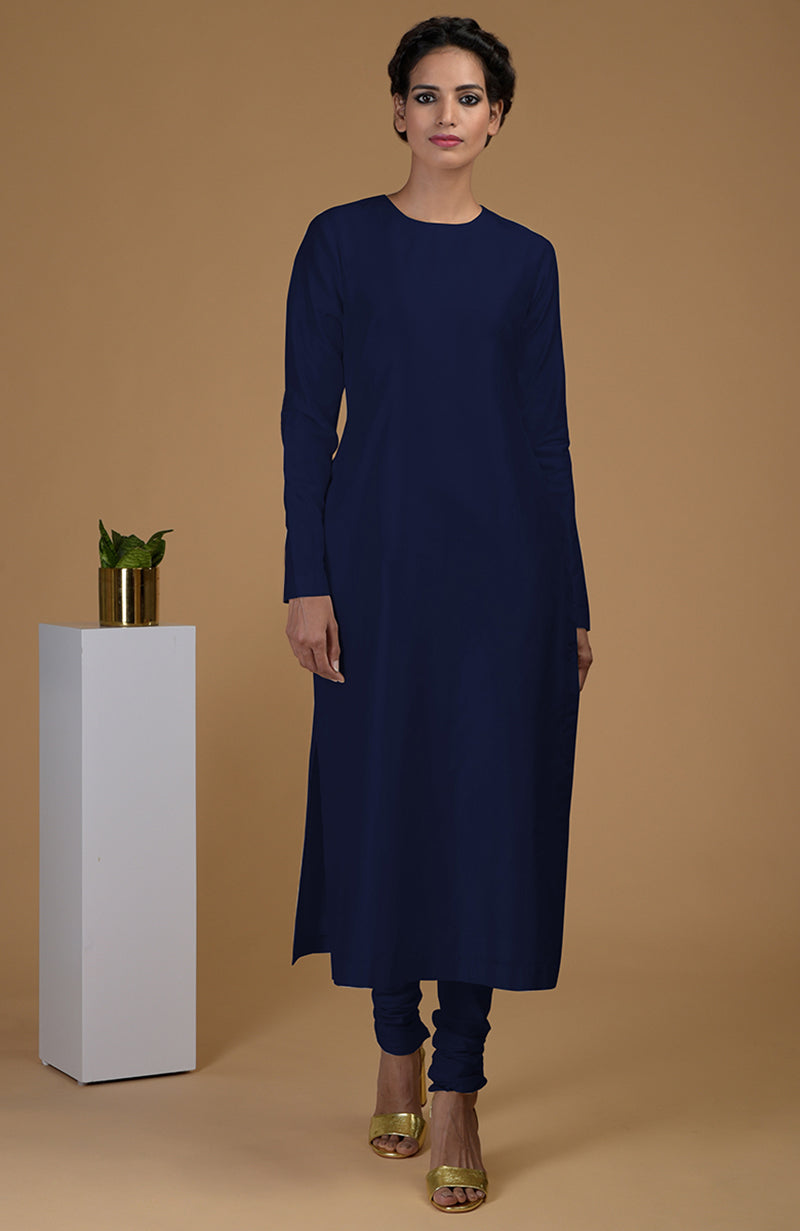 A woman models a navy blue pure Matka silk jewel neck kurta set with gold heels.