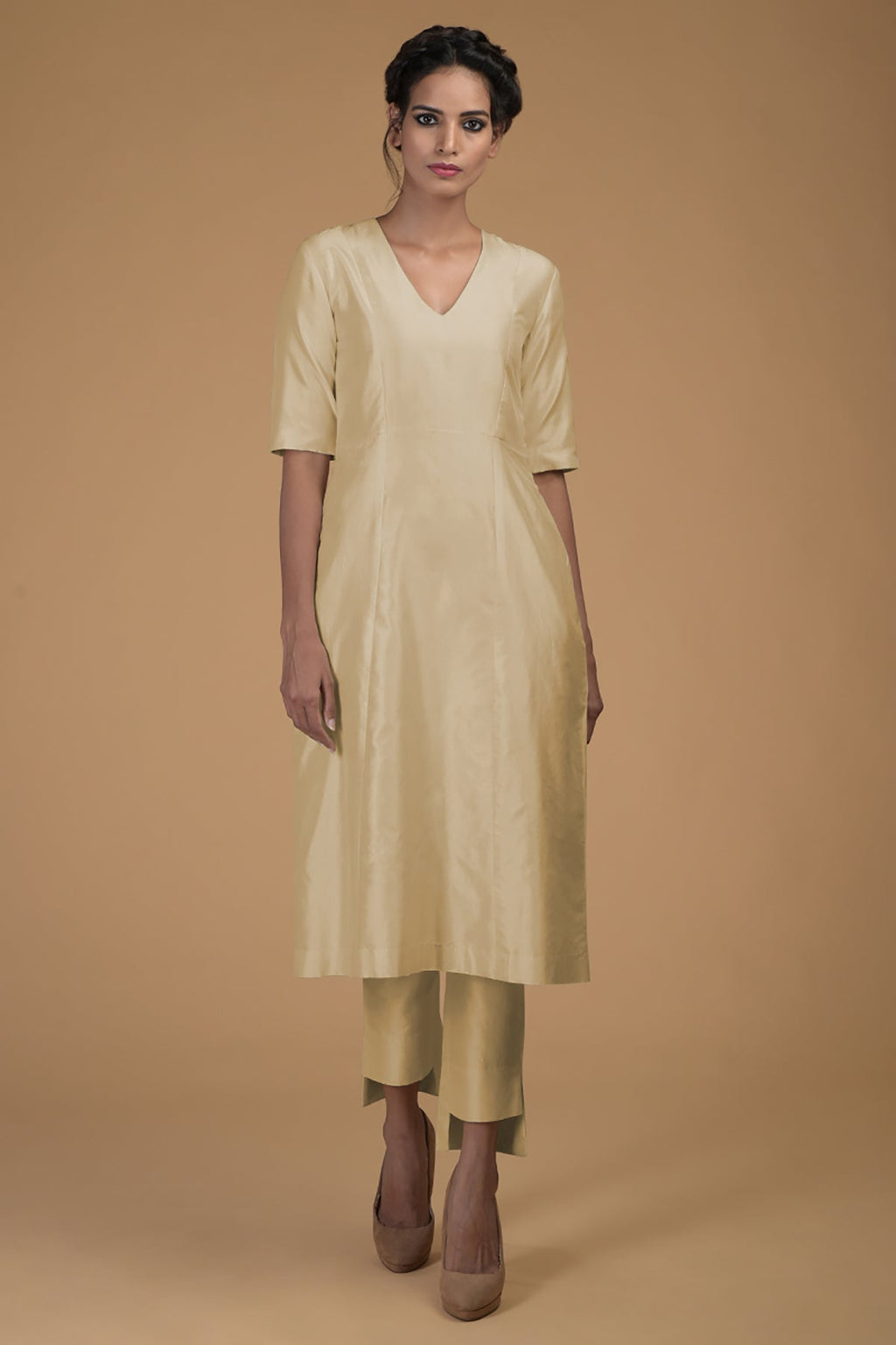 A woman models a beige pure Matka silk V-neck kali kurta set with slim pants.