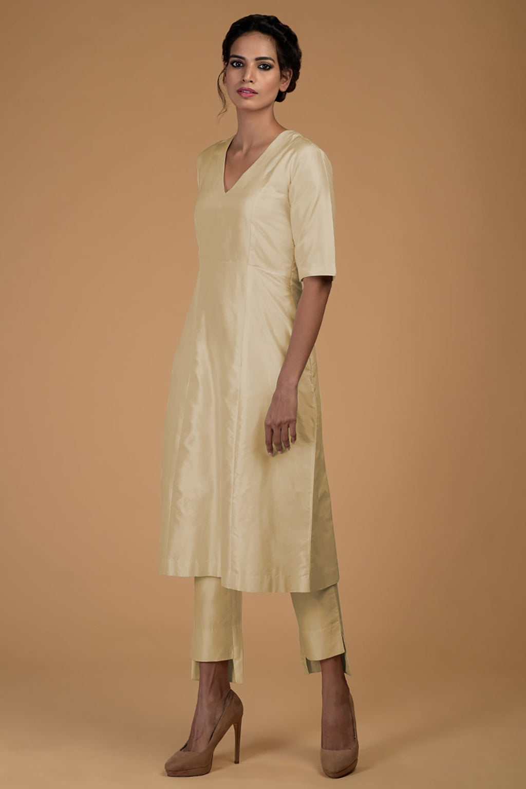 A woman models a beige pure Matka silk V-neck kali kurta set with slim pants.