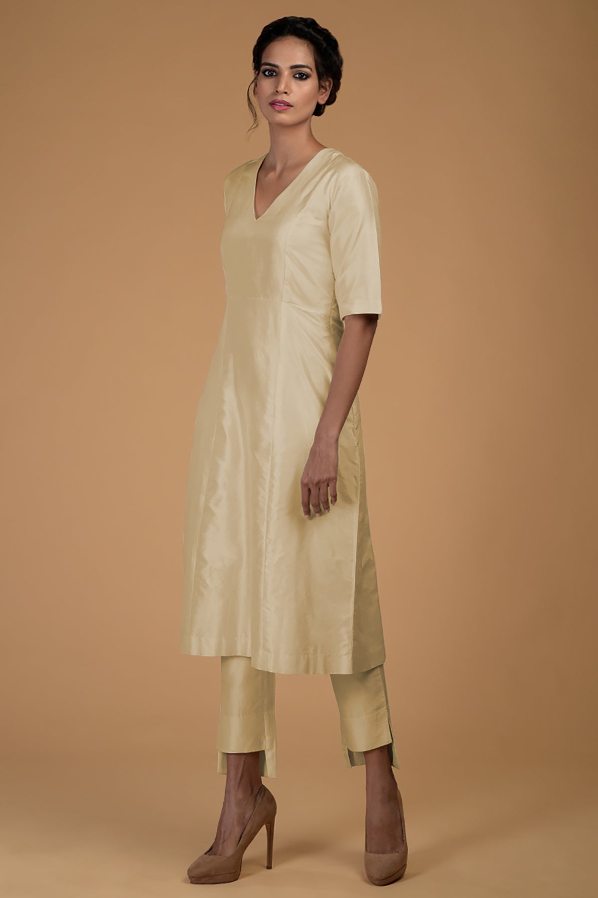 A woman models a beige pure Matka silk V-neck kali kurta set with slim pants.