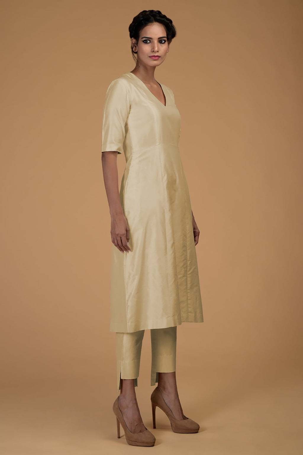 A woman models a beige pure Matka silk V-neck kali kurta set with slim pants.