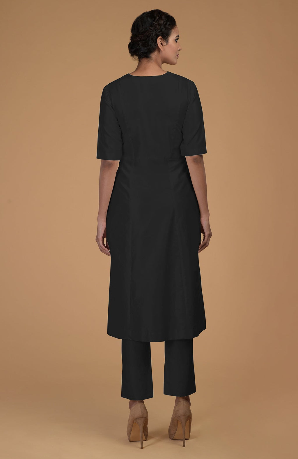 A woman from behind wearing a black V-neck kali kurta set and brown heels.