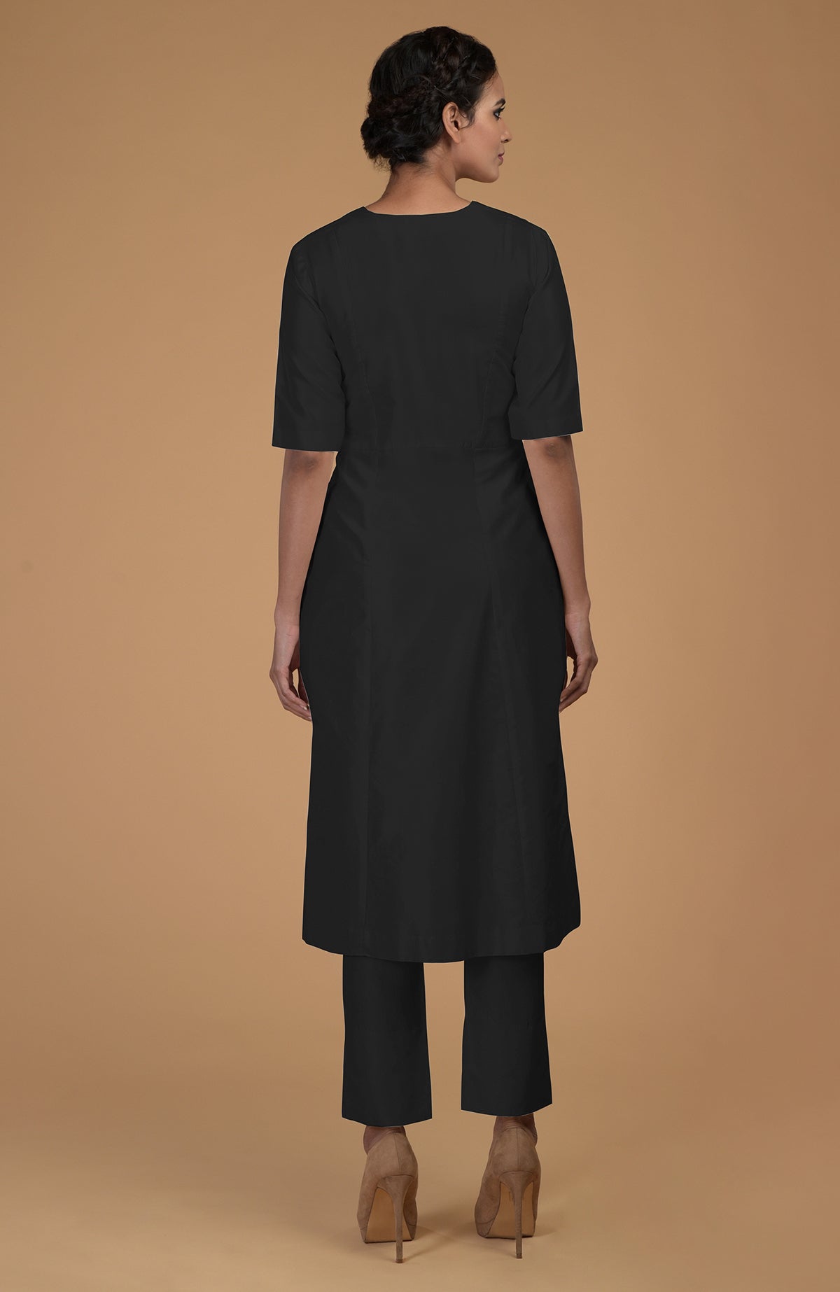 A woman from behind wearing a black V-neck kali kurta set and brown heels.