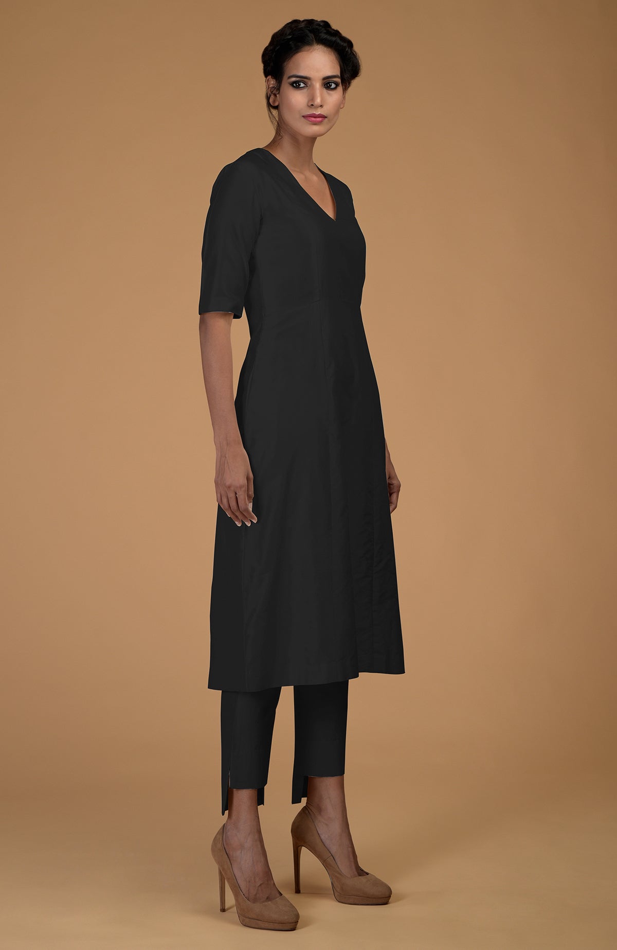 A woman models a black Matka silk V-neck kali kurta set with slim-fit pants and heels.