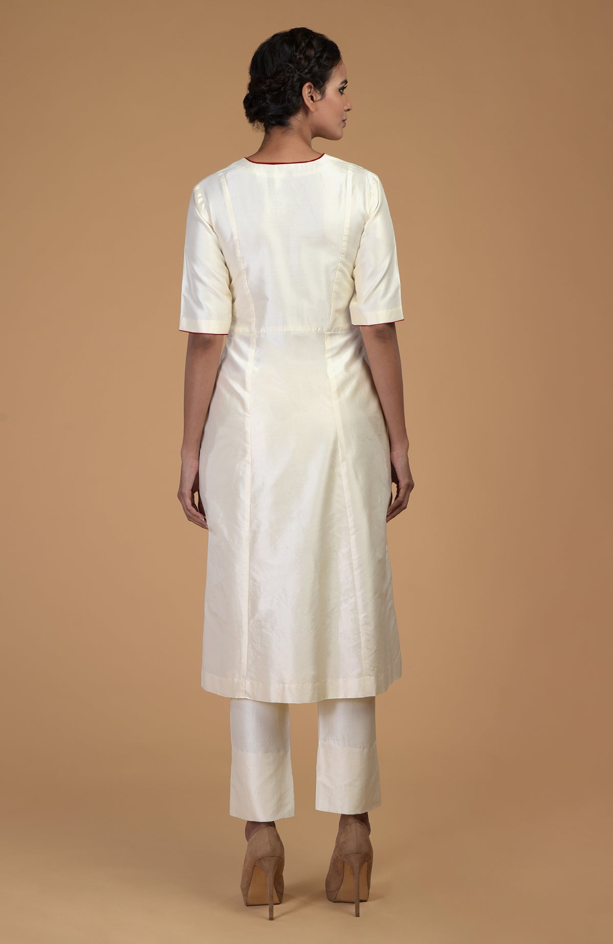 A woman models an ivory pure Matka silk V-neck kali kurta set with brown heels.
