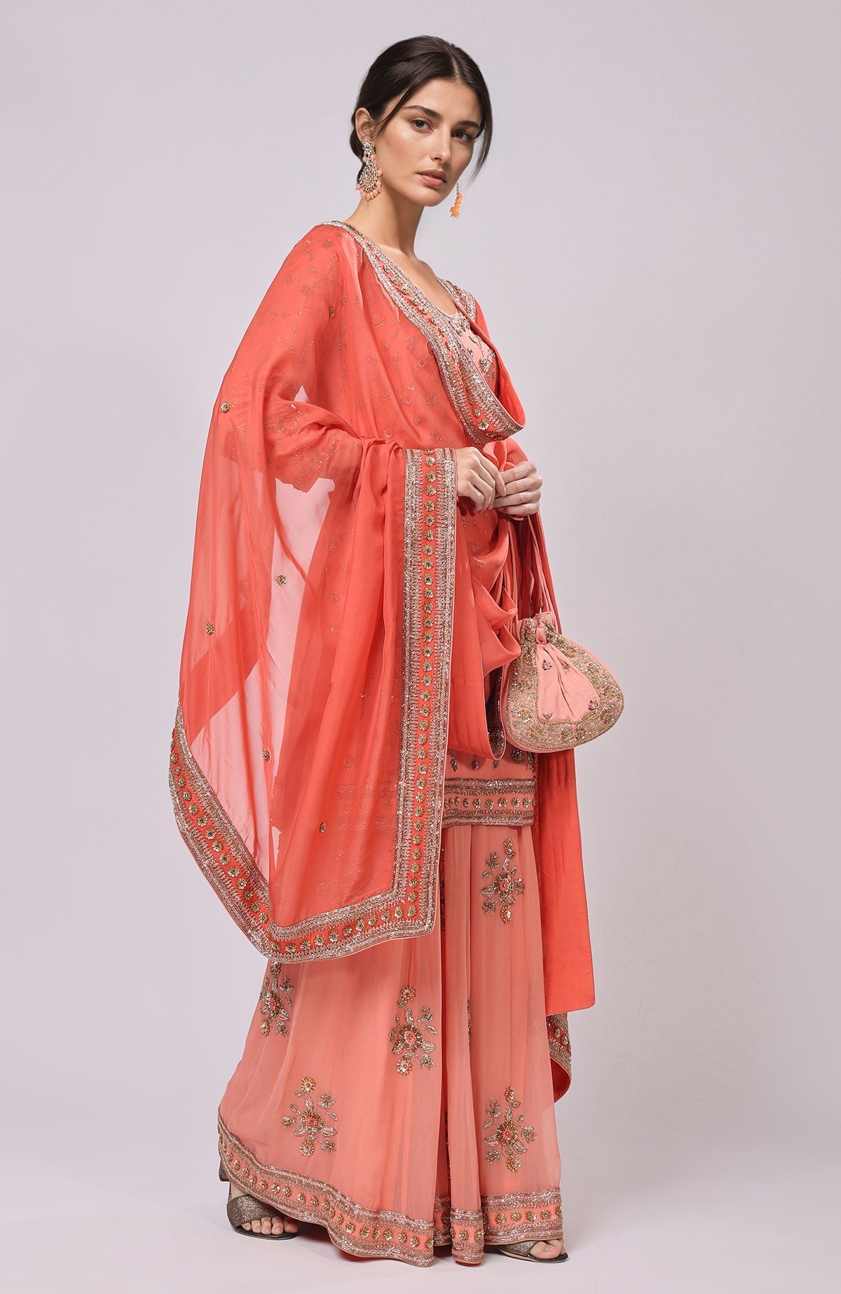 A model wears a salmon dabka and zardozi hand-embroidered sharara set with a matching potli bag.