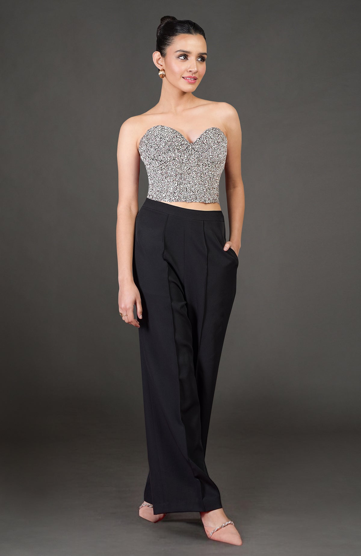 A woman models a strapless, sweetheart-neckline corset with black pants and embellished heels.