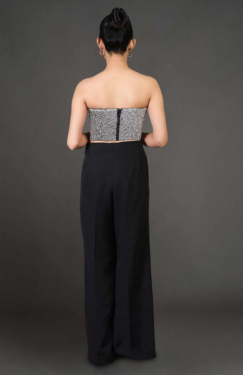 A woman from behind wears a silver sequined strapless top and black wide-leg pants.