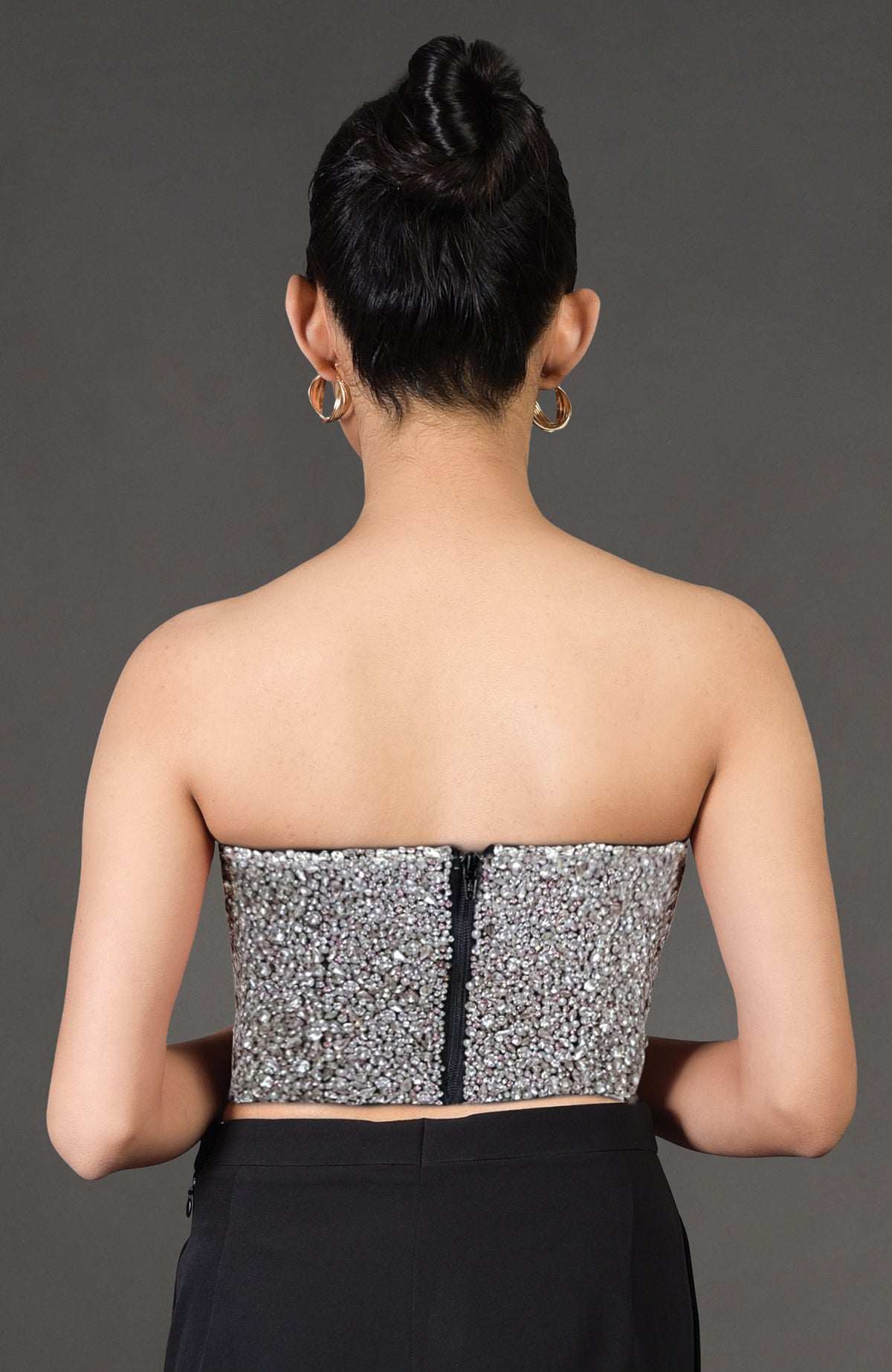 Back view of a woman wearing a strapless, crystal-embroidered corset with a visible zipper.