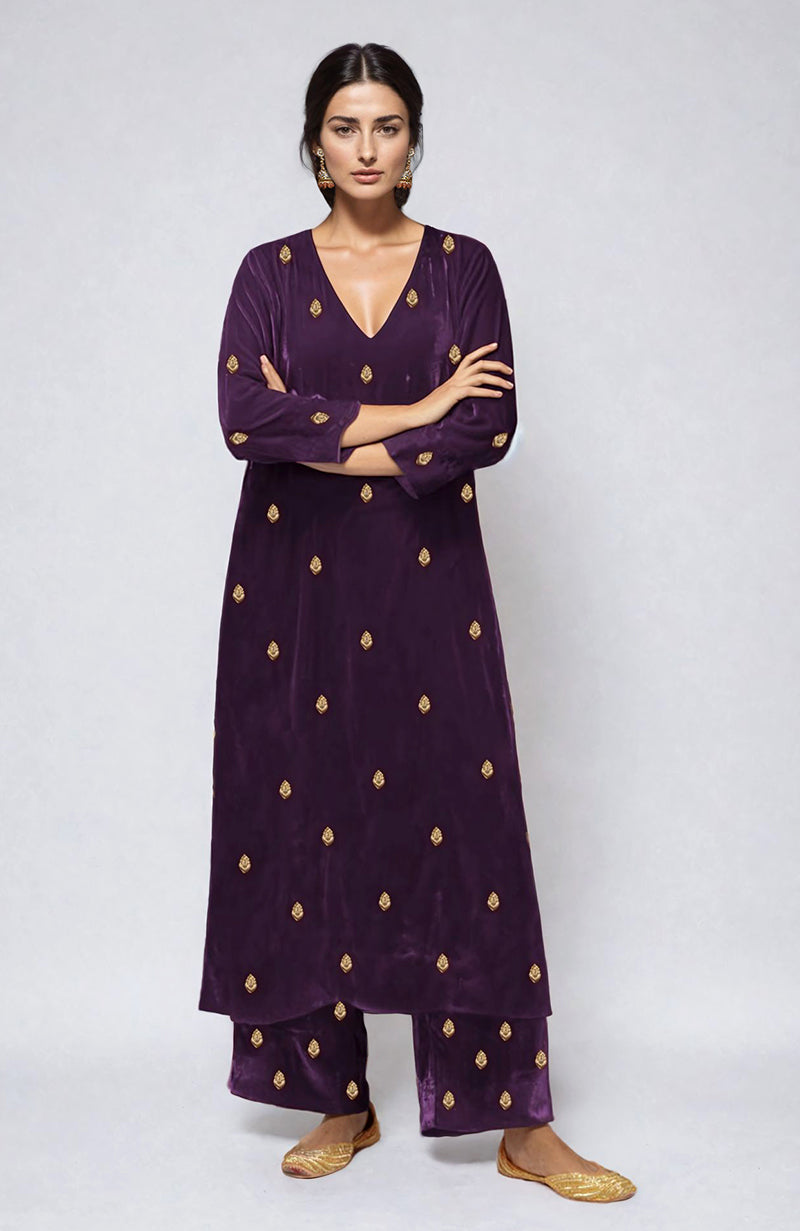 A woman models a purple velvet kurta set with gold embroidery.