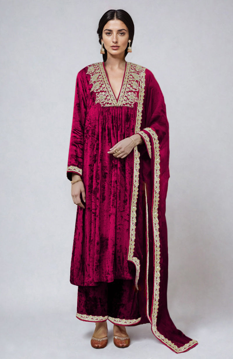 A woman models a bright rose gold velvet kurta set with gold embroidery.