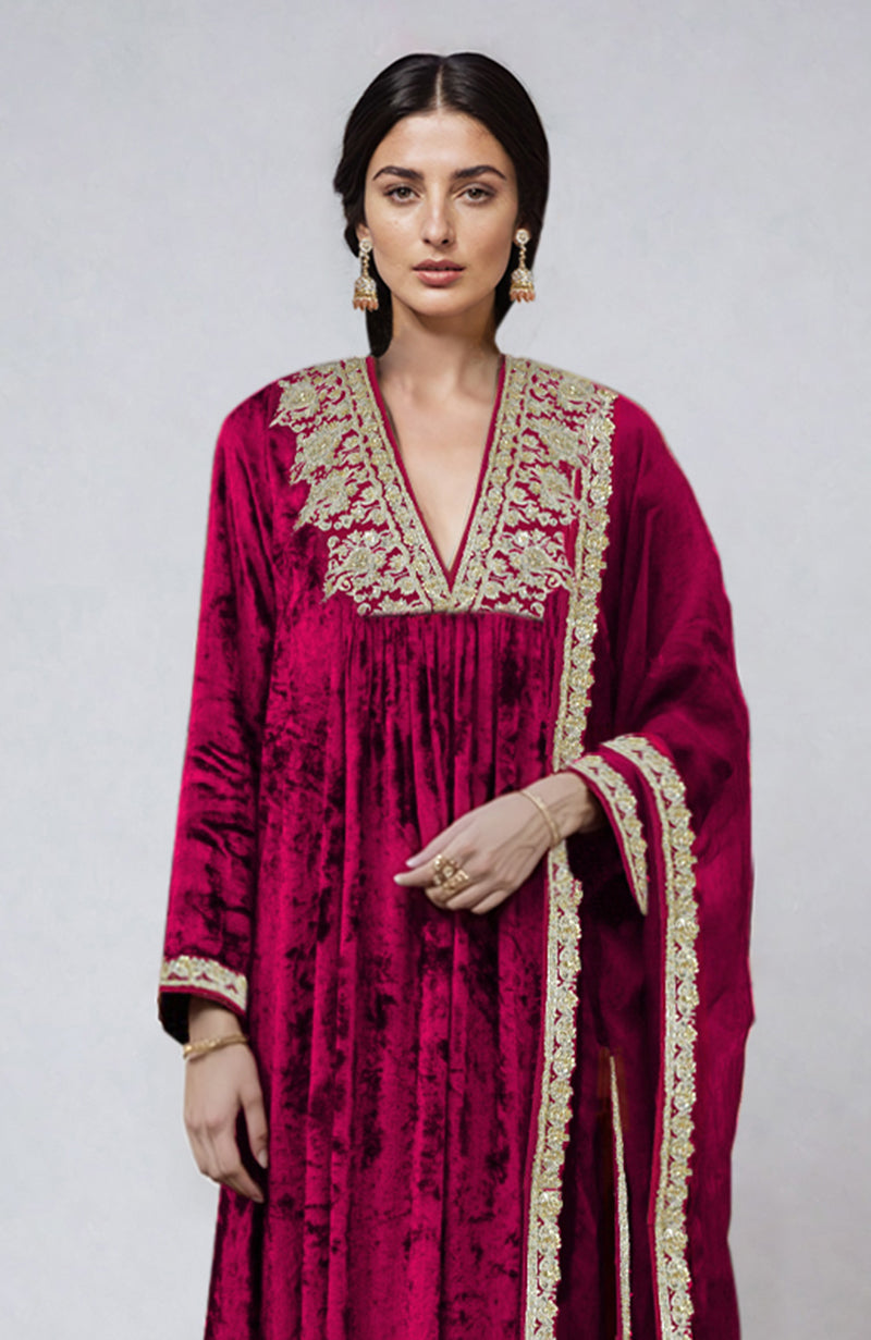 A woman models a bright rose gold velvet kurta set with intricate gold embroidery.