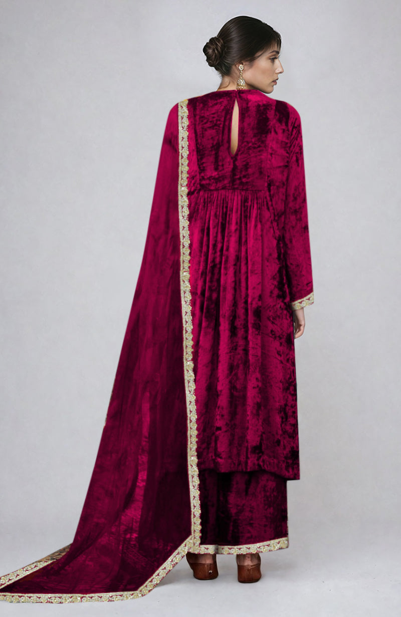 A woman from behind wears a bright rose gold velvet kurta set with gold embroidery.