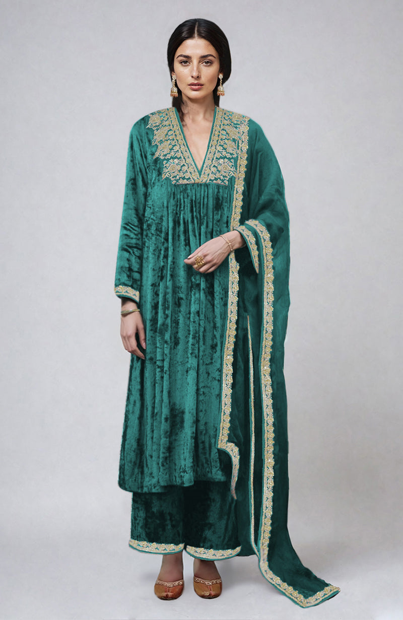A woman models a teal velvet kurta set with gold embroidery.