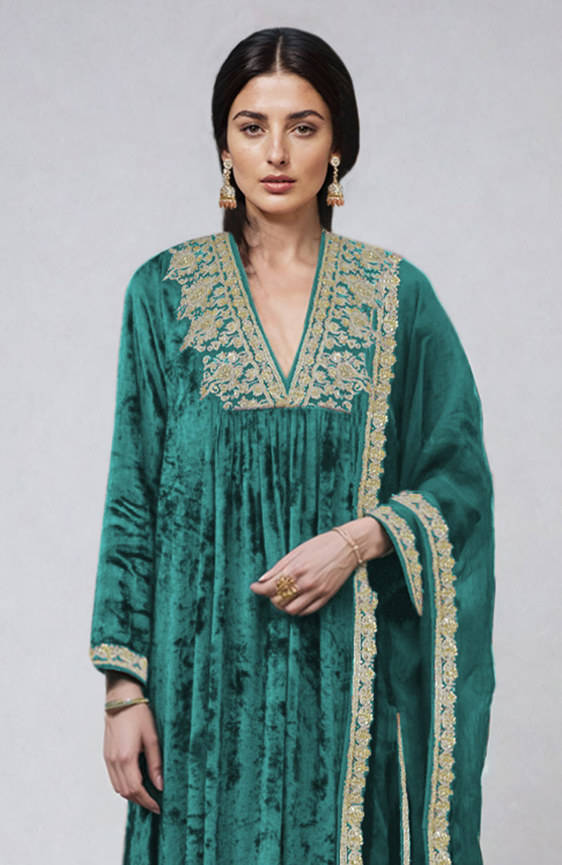 A woman models a green velvet kurta set with gold embroidery.