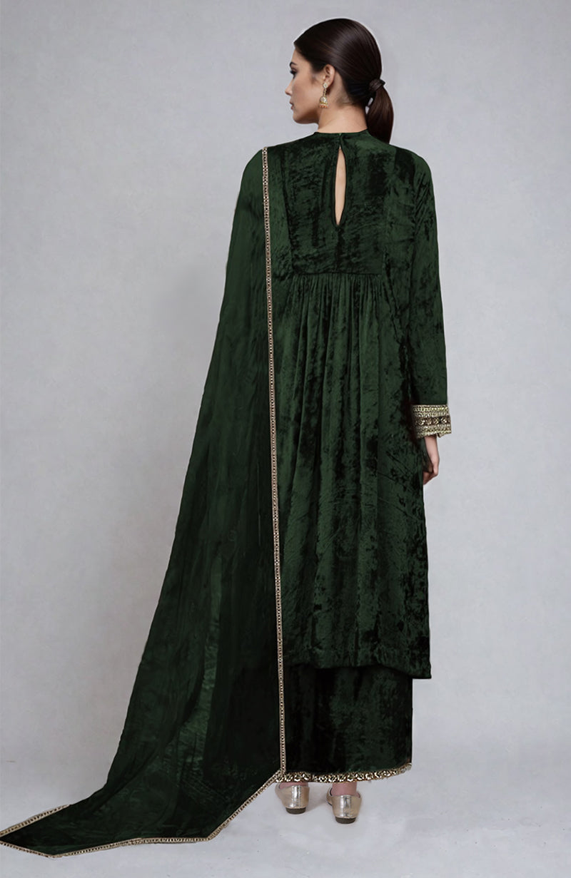 A woman models a bottle green velvet kurta set with gold embroidery.