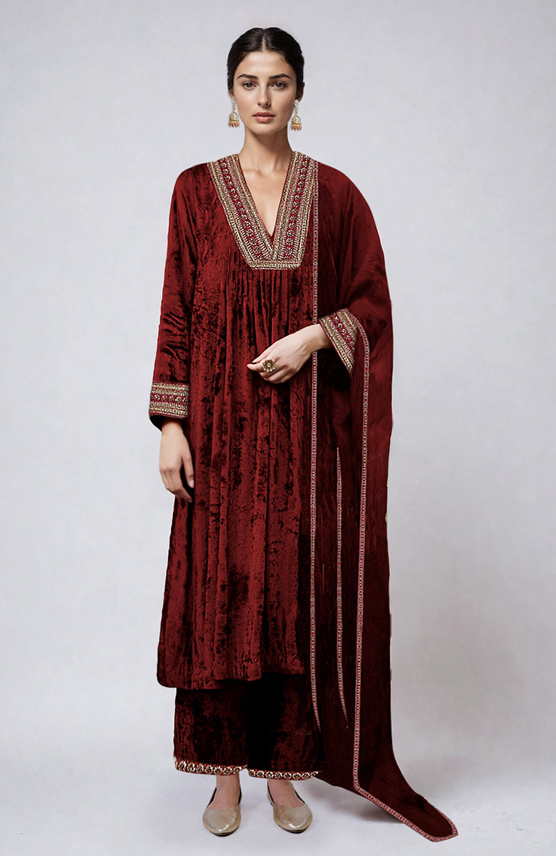 A woman models a maroon velvet kurta set with gold zardozi embroidery.