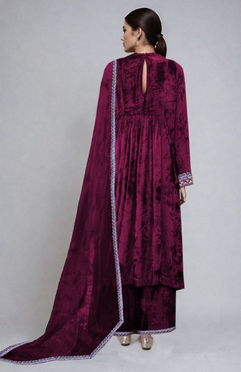 A woman models a bright rose velvet kurta set with a matching dupatta.