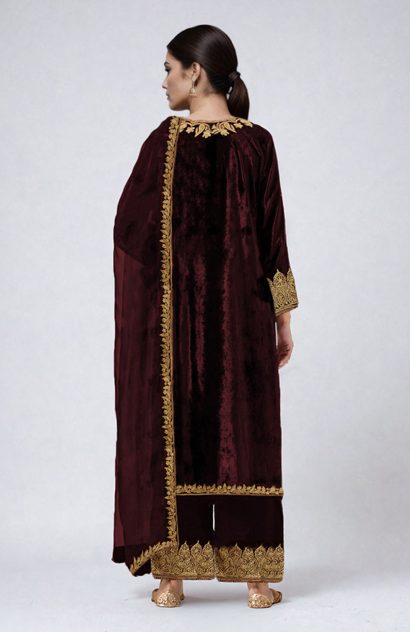 A woman models a maroon velvet palazzo set with gold Kashmiri embroidery from the back.