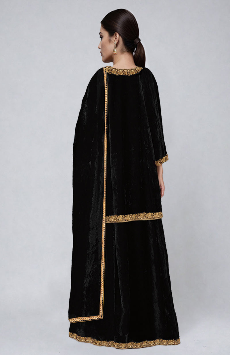 A woman from behind wears a black velvet sharara set with gold embroidery.